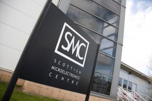 Photo from outside of the Scottish Microelectronics Centre. The logo board is in the foreground and the building in the background.